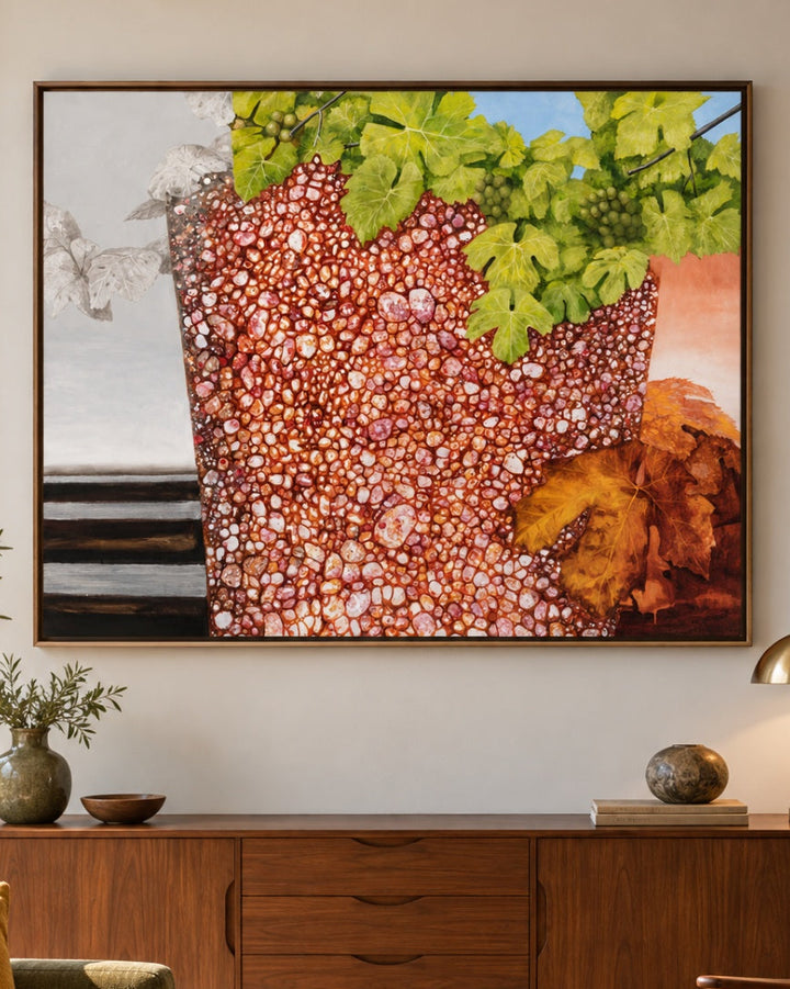 A framed abstract painting featuring a textured reddish-brown pot with green leaves and orange-brown rocks, displayed on a light gray wall above a mid-century modern wooden sideboard in a styled living room.