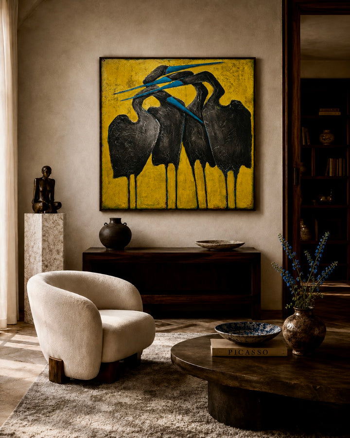 Living room with a beige armchair, round wooden coffee table, and a large abstract painting of birds on a yellow background.