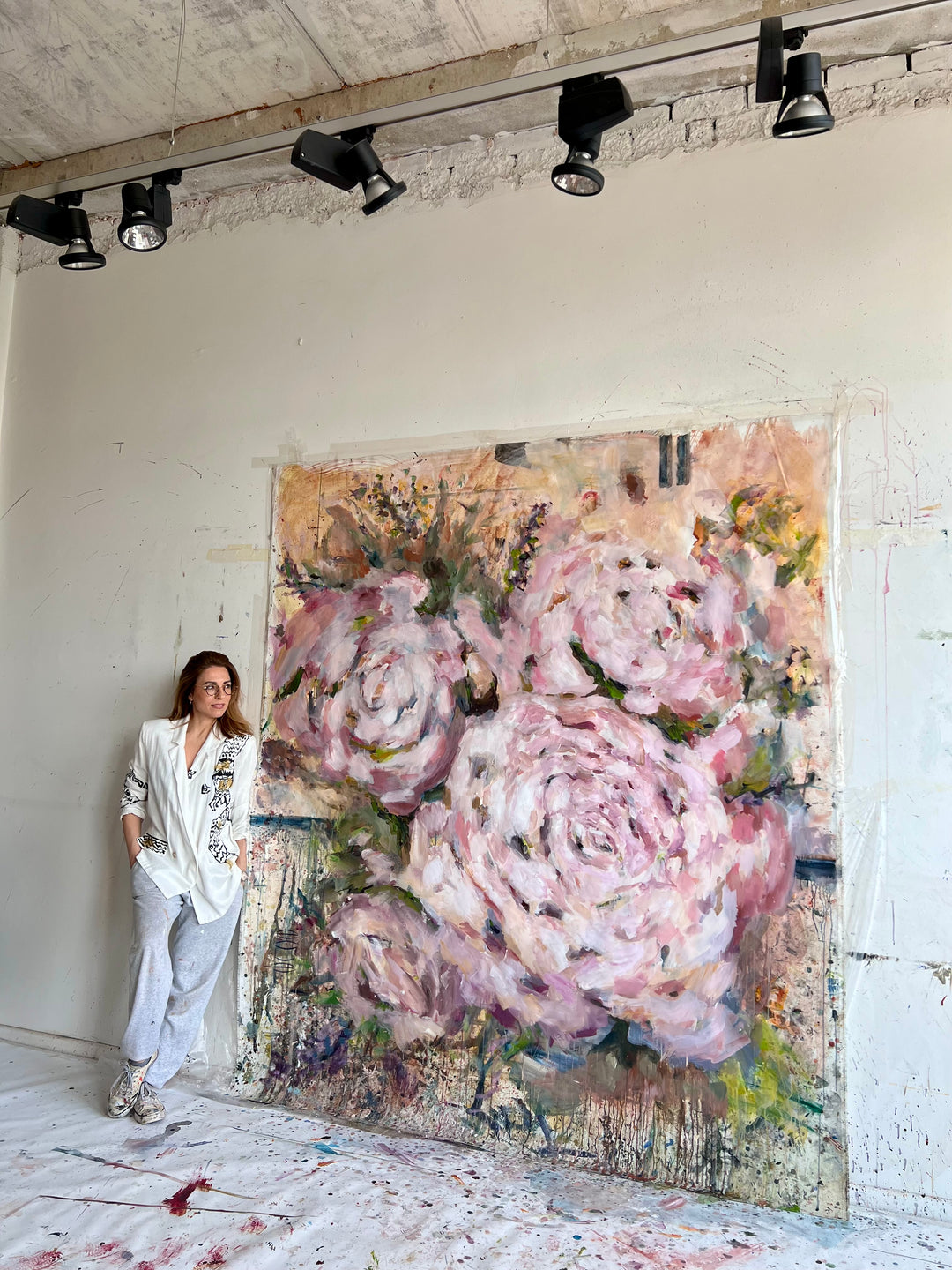 Person standing next to a large floral painting in an artist's studio.