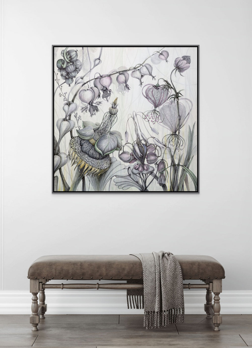 Framed botanical artwork on a wall above a wooden bench with a blanket.
