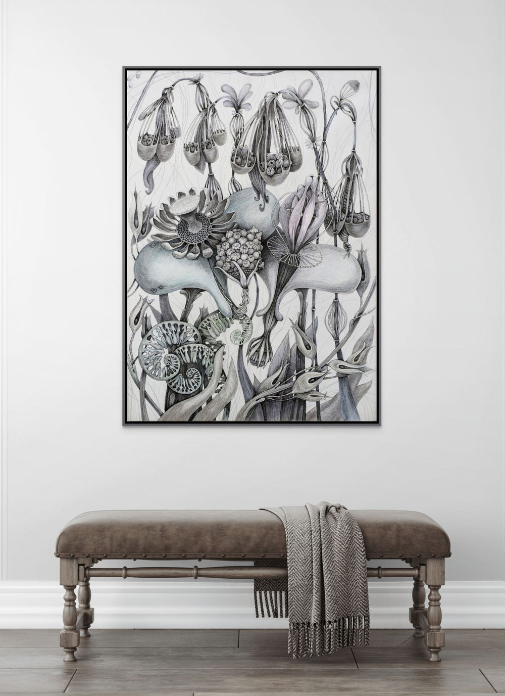 Framed botanical artwork on a wall above a bench with a blanket.