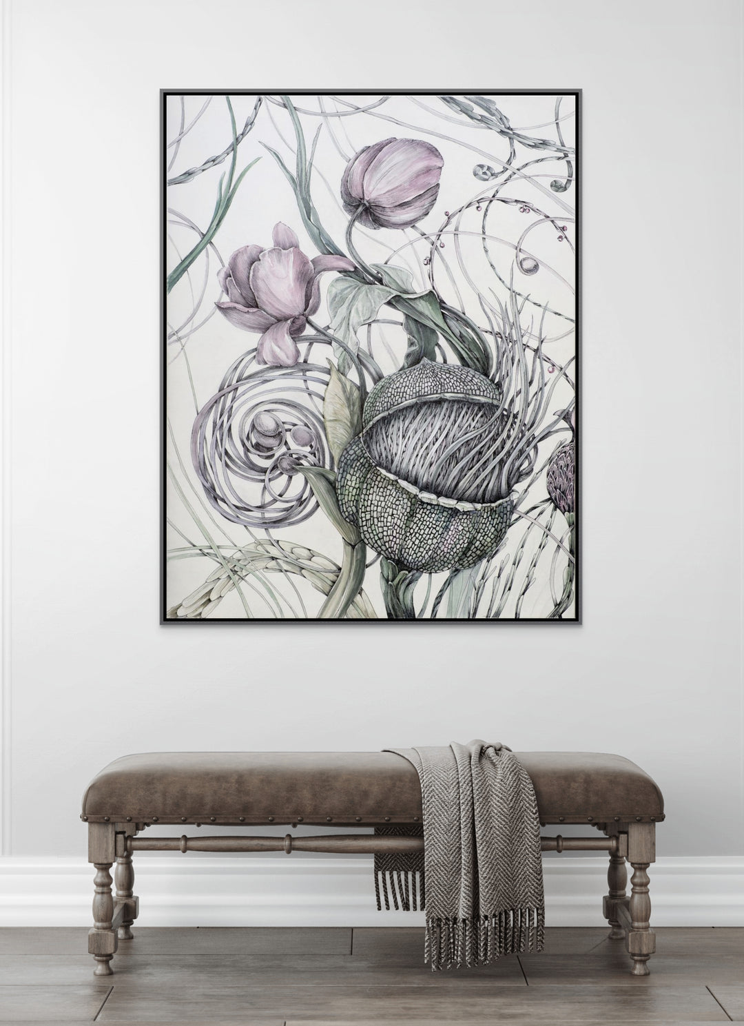 Framed botanical artwork on a wall above a bench with a blanket.
