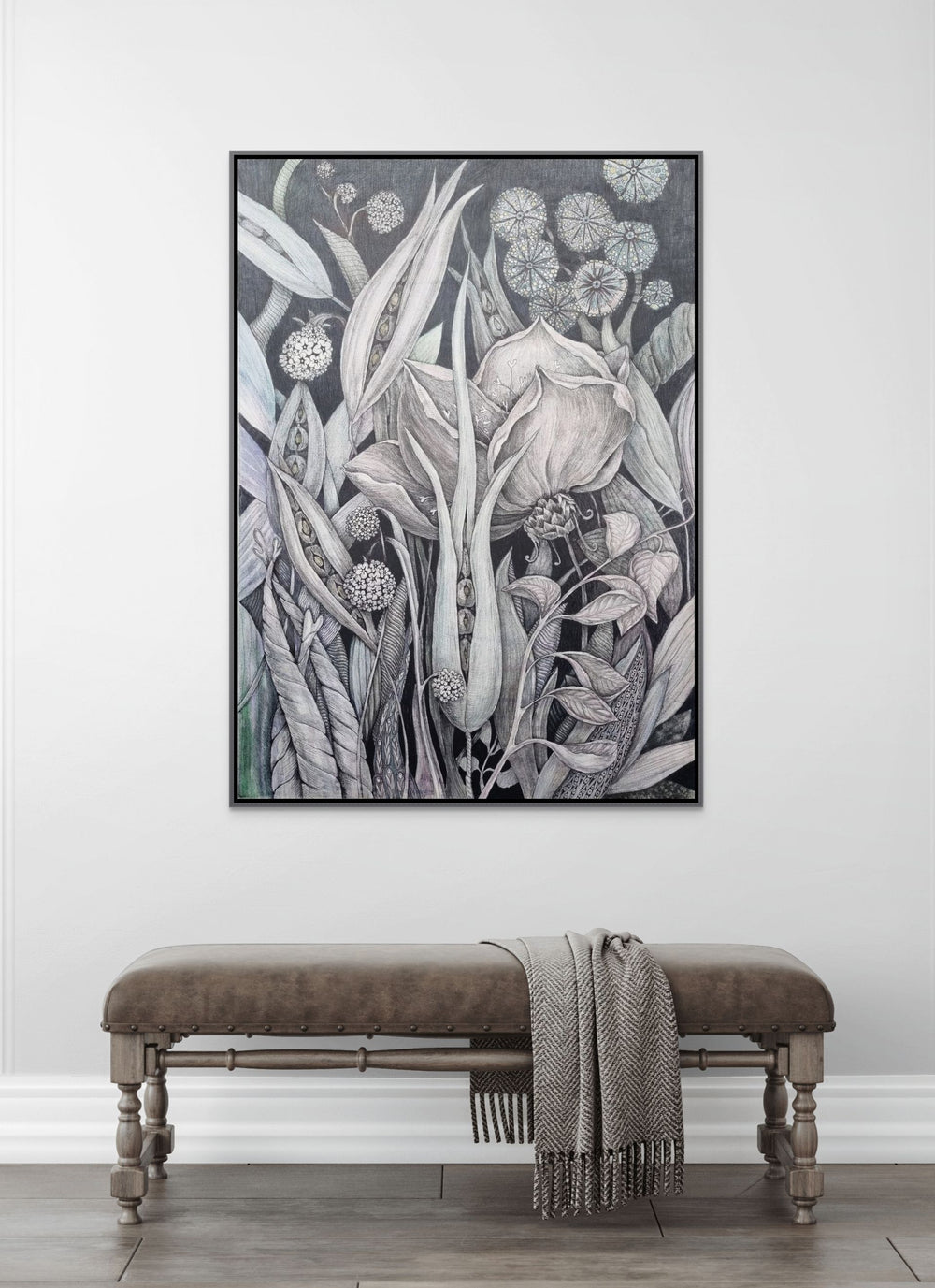 Framed botanical artwork on a wall above a bench with a blanket.