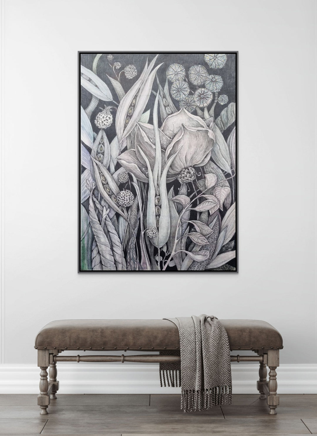 Framed botanical artwork on a wall above a bench with a blanket.