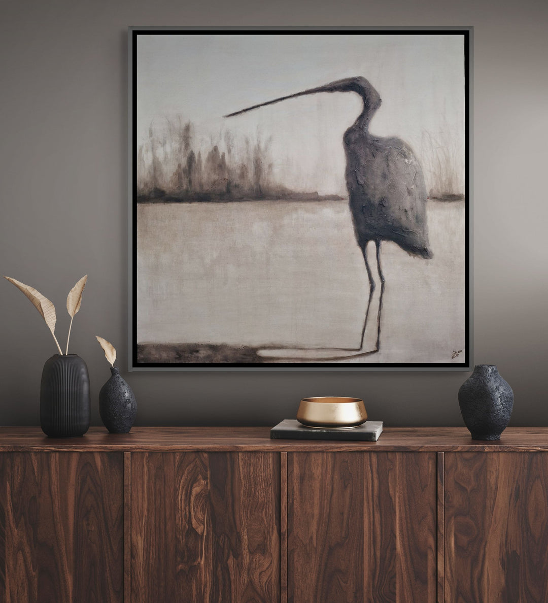 Framed artwork of a heron on a wall above a wooden console table with decorative items.